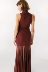 Vestido largo color beige, con cuello alto y sin mangas. La parte superior es ajustada al cuerpo y la falda es amplia y fluida, con paneles traslúcidos.