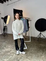 Sweater tejido en lana italiana con alpaca y viscosa, color crudo, con cuello alto y mangas largas. Diseño con trenzas en el frente y mangas. Corte holgado.