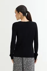 Cárdigan negro de tejido de punto fino con escote en V, cierre frontal con botones dorados y mangas largas con puños ajustados.