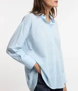 Camisa celeste de voile, corte oversized, con cuello clásico, cierre frontal con botones, mangas largas con puños largos y proceso de producción sostenible.