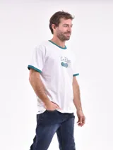 Remera blanca de manga corta con cuello redondo y ribete verde en cuello y mangas. Estampado frontal con texto "Court Classics" y diseño de pelotas de tenis.