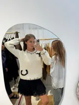 Buzo de lana merino tejido a mano en color crudo, con diseño de herradura y pespuntes decorativos en color negro. Presenta cuello redondo, mangas largas y un calce relajado.