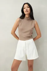 Top sin mangas color beige, de cuello alto y tejido de punto acanalado.