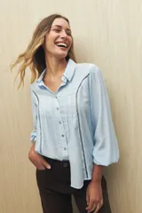 Camisa blanca de manga larga con cuello clásico y botones de nácar. Presenta detalles calados en el frente.