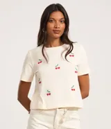 Remera color crema de algodón con bordados de cerezas rojas y hojas verdes.