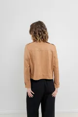 Chaqueta color beige de tela tipo gamuza con elastano, cuello solapa, manga larga con trabillas en hombro, bolsillos delanteros con cremallera metálica y cierre frontal con cremallera.