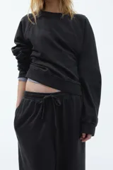 Pantalón deportivo negro de corte holgado, con cintura elástica y cordón ajustable. Confeccionado en felpa de algodón liviano con efecto lavado, bolsillos laterales y bajos sin rematar.