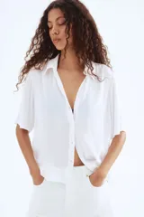 Camisa blanca de viscosa con efecto arrugado, de manga corta, corte holgado, cuello clásico, botones frontales y canesú con pliegue de caja en la espalda.