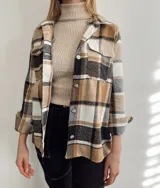 Sobrecamisa a cuadros color marrón, blanco y negro, con cuello camisero, cierre frontal con botones metálicos, dos bolsillos con solapa en el pecho y mangas largas con puños abotonados.