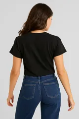 Remera cropped negra de algodón con cuello redondo y estampado de hojas blancas en el hombro.