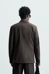 Blazer negro de corte relaxed fit, confeccionado en tejido de algodón con acabado ligeramente encerado. Tiene cuello con solapas de muesca, manga larga con puños abotonados, bolsillo de vivo en el pecho, bolsillos de solapa en la cadera, bolsillo interior, aberturas en la espalda y cierre frontal con botones.