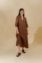 Vestido largo color beige, confeccionado en lino, con escote en V con volados y apliques de puntilla en las mangas. Posee bolsillos delanteros y tajos laterales.
