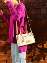 Cartera bandolera de cuero crudo con forro de tela, bolsillo frontal y bolsillo interno. Tiene correa larga regulable y manijas cortas de cuero marrón.