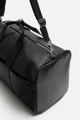 Bolso de viaje negro con compartimento principal con cierre de cremallera, bolsillo interior con cremallera, detalle de arnés en la parte frontal, dos asas de mano y asa de hombro ajustable y extraíble.