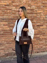 Cartera bandolera de cuero color marrón chocolate, con forro de tela y herrajes dorados. Tiene doble asa de mano y correa larga regulable y desmontable. Incluye bolsillo frontal con cierre y bolsillo interno.