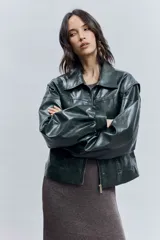 Cazadora corta de efecto piel color verde oscuro, con cuello solapa, cierre frontal de cremallera y mangas largas abullonadas con puños elásticos.