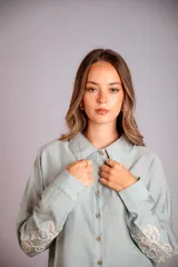 Camisa celeste de corte clásico, con botones frontales y bordados florales en las mangas.
