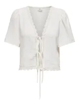 Top blanco con textura, escote en V, mangas cortas abullonadas y cierre con lazos. Detalle de encaje en escote y ruedo.