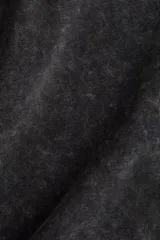 Remera de algodón con efecto acid wash en color negro o gris oscuro, corte oversize y cuello redondo acanalado con argollas metálicas decorativas.