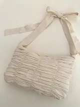Cartera de hombro color crudo, confeccionada en algodón con diseño drapeado y manijas regulables mediante un moño.