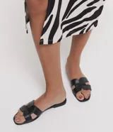 Sandalia plana de cuero sintético color negro, con puntera cuadrada y tiras anchas en forma de H.