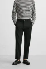 Pantalón slim fit negro confeccionado en tejido con elasticidad en ambas direcciones. Cuenta con bolsillos frontales y traseros de vivo con botón. Cierre frontal con cremallera y botón.