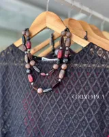 Conjunto de collares de cuentas de diferentes colores y materiales, incluyendo cuentas de piedra, madera y cristal. Los collares tienen cadenas doradas y etiquetas blancas con la marca "MANDRA".