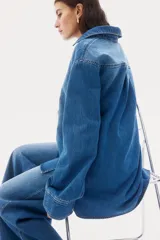 Camisa de denim azul con cuello abierto y canesú con pliegue de caja en la espalda. Modelo de corte holgado con hombros caídos y mangas largas con botones a presión en los puños. Bajo recto, algo más largo atrás, con aberturas laterales.