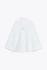 Camisa blanca oversize de popelina de algodón, con cuello solapa, manga larga con puños y cierre frontal con botones ocultos. Detalle de hilo de contraste en los botones.