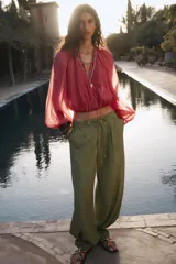 Pantalón ancho color verde oliva confeccionado en lino. Tiro alto con cintura elástica ajustable con cordón y pinzas delanteras. Presenta bolsillos laterales y traseros. Incluye cinturón de la misma tela con apliques metálicos.