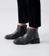 Botín de cuero negro con elásticos laterales, punta cuadrada y tacón bloque de madera. Presenta cierre lateral interno y suela de goma.