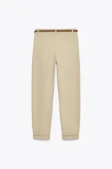 Pantalón chino color amarillo claro, de tiro medio, con bolsillos frontales y traseros. Incluye cinturón trenzado marrón.