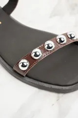 Sandalias bajas de cuero color marrón con apliques de tachas metálicas plateadas.