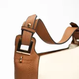 Cartera tipo hobo de cuero sintético color crema con laterales y asa corta color marrón.