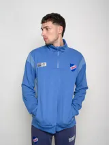 Buzo azul de felpa con medio cierre, cuello alto y mangas largas. Presenta el escudo del Club Nacional de Football en el pecho y el logo de Umbro en la manga.