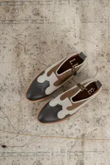 Botines de cuero marrón y blanco con diseño western, puntera redondeada y cierre lateral con cremallera. El talón tiene una tira de cuero para facilitar el calce.