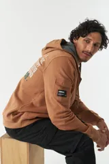 Campera marrón de felpa con capucha y cordón ajustable, lettering estampado en la espalda, bolsillo en la manga, puños y logo en grifa de goma.