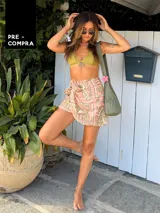 Falda pareo corta, color rosa pálido con estampado en tonos dorados/beige, con diseño de conchas y motivos geométricos. Se anuda en la cintura.