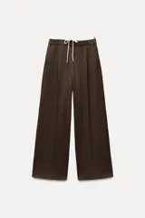 Pantalón marrón de tiro alto con doble cintura elástica ajustable con cordón, pinzas frontales, bolsillos delanteros y falso bolsillo de vivo en espalda.