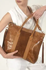 Bolso tipo tote de cuero vacuno grabado croco color whisky, con paneles de gamuza y detalles en napa whisky. Tiene doble asa rígida, correa desmontable regulable, cierre superior con cremallera y flecos laterales.