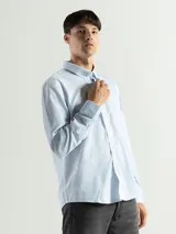 Camisa celeste y blanca a rayas verticales, de manga larga y corte clásico. Tiene cuello abotonado y bolsillo en el pecho.