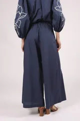 Pantalón ancho de algodón color celeste claro, con bordados de flores blancas en los bajos. Presenta un corte de tiro alto con pliegues frontales y cierre de botón visible.