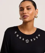 Remera negra de viscosa con cuello redondo y mangas cortas. Presenta apliques de strass en el escote.