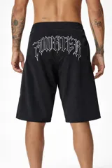 Short de baño negro con cordón de ajuste blanco en la cintura. Presenta un estampado vertical de figuras abstractas en color violeta y un logo estilizado en blanco en el lateral derecho. En el ruedo inferior izquierdo tiene un pequeño logo circular y una estrella de cinco puntas.