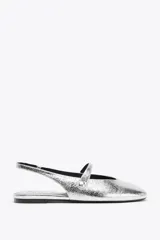 Zapato tipo bailarina destalonada plateada con efecto metalizado, punta redonda y tira delantera con aplique metálico.