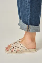 Sandalias color beige de cuero vacuno, con tiras entrelazadas y tachas redondas plateadas.