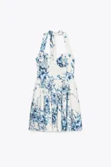 Vestido corto blanco con estampado de flores azules, cuello halter ajustable con lazadas y espalda descubierta.