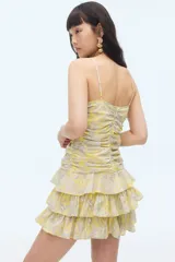 Vestido corto amarillo con estampado paisley, escote en V, breteles finos ajustables y falda escalonada con volados. Presenta un cierre oculto en la espalda y forro interior.