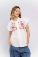 Camisa blanca de mangas cortas con volados y bordado de flores en el frente.