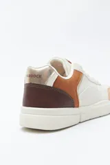 Zapatilla urbana blanca de mujer, con silueta moderna y líneas limpias. Presenta detalles en poliuretano liso y un panel plateado en el talón. La suela es de perfil recto y firme.